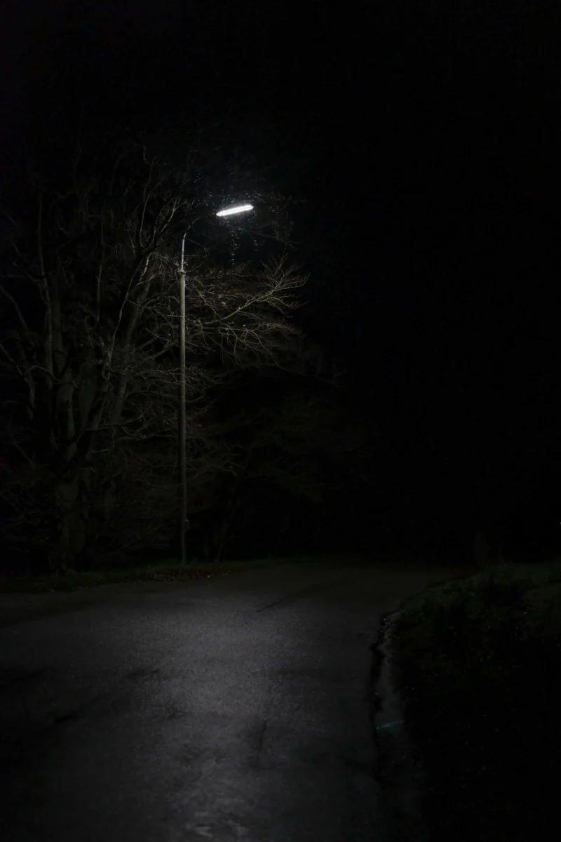 AMOled darkview of an empty asphalt road illuminated by a single glowing light post under a pitch-black night sky in 4K resolution.